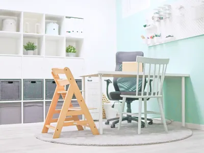 Blick auf Tisch mit 2 Stühlen und einem Kinderstuhl. Im Hintergrund steht ein Regal mit grauen und weißen Körben und zwei Topfplfanzen.